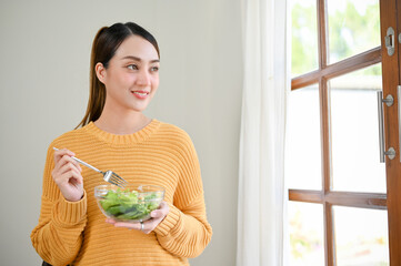 Attractive Asian woman standing in the living room, holding a salad bowl