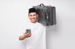 © Bangun Stock Photo - Smiling young Asian Muslim man carrying a suitcase and holding mobile phone isolated on white background. Ramadan and eid Mubarak concept