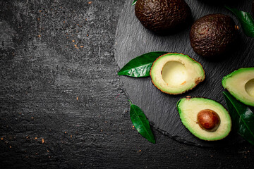 Wall Mural - Pieces of fresh avocado with leaves on a stone board. 