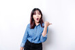 © Reezky - Shocked Asian woman wearing blue shirt pointing at the copy space beside her, isolated by white background