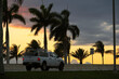 Dark palm trees against sunset sky and driving car on seaside street on summer Florida evening