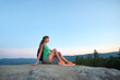 Hiker girl resting on rocky mountain top enjoying morning nature during her travel on wilderness trail. Lonely female traveler traversing high hilltop route. Healthy lifestyle concept