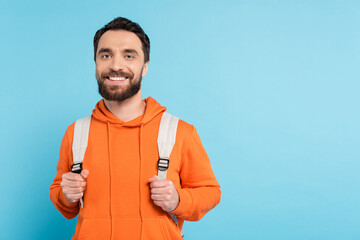 Wall Mural - happy bearded student in orange hoodie smiling at camera isolated on blue.