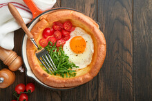 Dutch Baby Pancake. Fresh Homemade Dutch Baby Pancake With Fried Egg, Tomato And Green Arugula In Reed Cast-iron Pan On Old Wooden Table. Flat Lay, Close Up.
