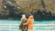 Back view of young traveling couple hugging on the ship and enjoying the beautiful view of mountains and cliffs.