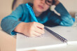 Small cute little boy taking notes while learning from home. Online education concept.