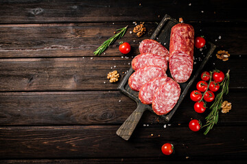 Poster - Pieces of salami sausage on a cutting board with cherry tomatoes and rosemary.