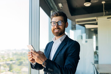 Wall Mural - Business and telecommuting concept. Portrait of happy middle aged man using smartphone, texting with client in office