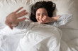 © Prostock-studio - Cheerful pretty young european woman wakes up, waves her hand or closes from camera, lies on white bed