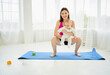 Mother on maternity leave squats on yoga mat with baby in her arms, sports after the birth of baby