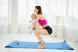Young mom on maternity leave squats on yoga mat with baby in her arms. Sports at home after pregnancy