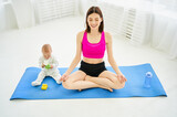 Fototapeta  - Cute smiling young mother with newborn baby meditating after exercising on yoga mat