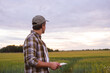 © Acronym - Farmer with a tablet computer in front of a sunset agricultural landscape. Countryside field. The concept of country life, food production, farming and technology concept.