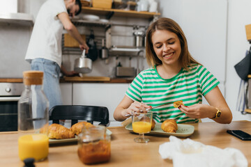 Wall Mural - Young caucasian woman eats croissant for breakfast