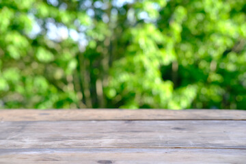 wooden table in garden, beautiful blurred natural landscape in background with green foliage and soft sunset transparenting through branches, concept cozy mood, blank for designer