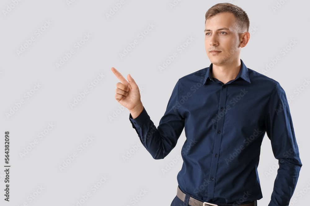 Young businessman in blue shirt pointing at something on light background