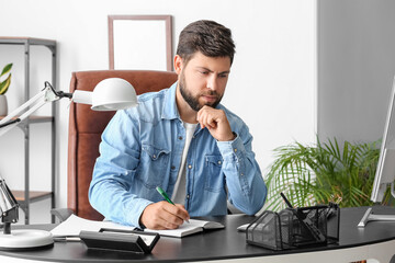 Wall Mural - Handsome young businessman working with notebook at table in office