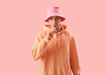 Wall Mural - Young man in bucket hat smoking disposable electronic cigarette on pink background