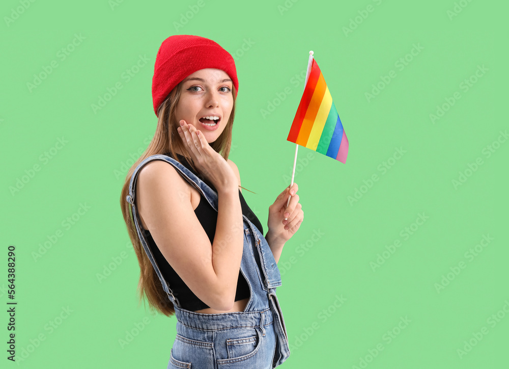 Surprised young woman with LGBT flag on green background