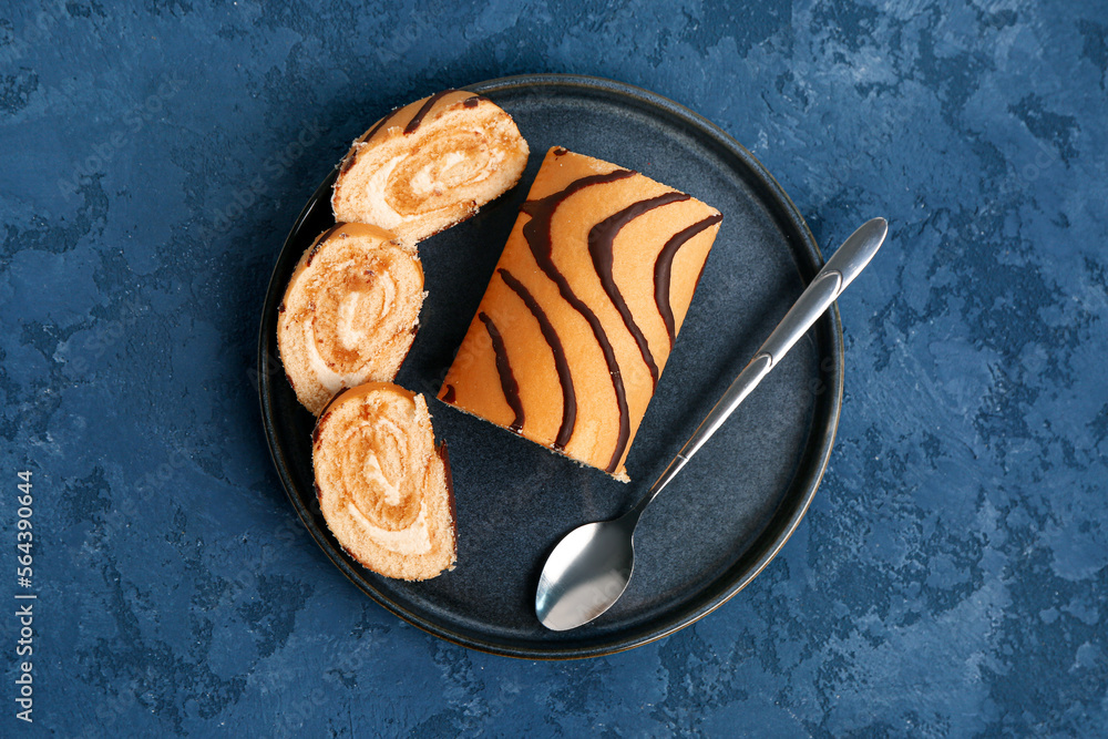 Plate with pieces of delicious sponge cake roll on blue table