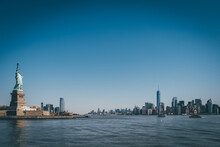 Statue Of Liberty In Front Of NY Skyline And Blue Skies