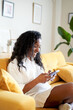 © CarlosBarquero - Vertical photo of a Cheerful Woman using mobile phone at home. African American smiling lady is laying on the sofa. High quality photo