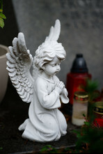 Small White Praying Angel Figure On A Grave With Grave Candles In Blurred Background