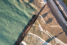 Beautiful Top Down Shot Of The Shoreline Of Lake Michigan With A Concrete Pier And Breakwater Diagonally Across The Frame With Sunshine Lighting Up The Sandy Shoreline And Turquoise Waters.
