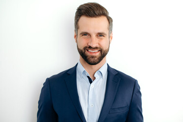 Close-up photo of a confident handsome bearded caucasian businessman, corporate executive, ceo, in formal elegant suit, stand on isolated white background, looks at camera, smiling friendly