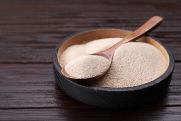 Wall Mural - Bowl and spoon with active dry yeast on wooden table, closeup. Space for text