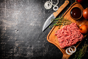 Canvas Print - Minced meat on a wooden cutting board with onions and sprigs of thyme. 