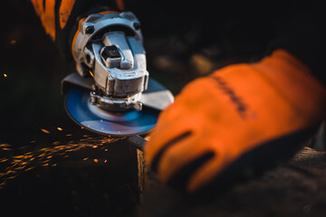 Wall Mural - The hands of the master saw the metal with a grinder. Metal works in the workshop close up. Metal processing with angle grinder. Sparks in metalworking.