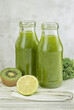 Green smoothie in glass bottles on gray background.