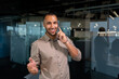 © Liubomir - A young African American man is standing in the office and talking on the phone. gesturing with his hands, looking at the camera, smiling.
