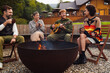 © Drobot Dean - Young friends drinking tea and playing guitar while sitting around campfire in nature