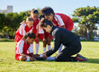 © Nina/peopleimages.com - Accident, injury and children soccer team with their coach in a huddle helping a girl athlete. Sports, first aid and kid with a sore, pain or muscle sprain after a match on an outdoor football field.