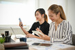 © bongkarn - Attractive Asian businesswoman using her mobile phone while working with her coworker