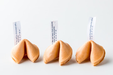 Three crispy fortune cookies in a row with fortune notes inserted.