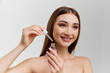© master1305 - Portrait of young beautiful girl with healthy skin posing with face serum, toner over grey studio background. Concept of natural beauty, skin care, cosmetology, cosmetics, health, plastic surgery