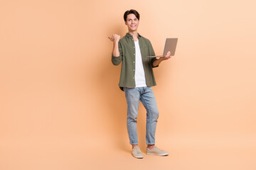 Wall Mural - Full body length photo of young man interested looking empty space pointing finger with netbook promotion ad isolated on beige color background