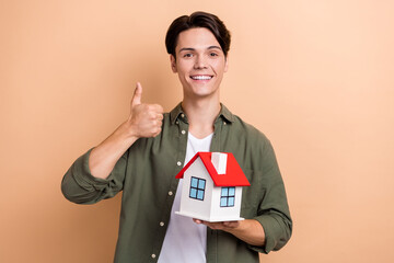 Sticker - Photo of young real estate agent entrepreneur wear stylish khaki shirt thumb up like hold new house good price isolated on beige color background