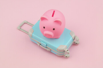 Travel budget concept. Piggy bank on travel suitcase on pink background.