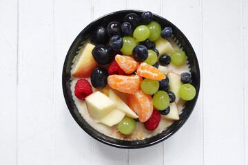 Fruit salad with porridge, healthy breakfast meal with copy space on white wood background