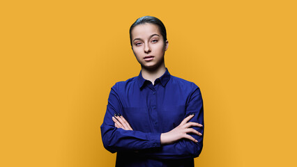 Young serious female with crossed arms on yellow background