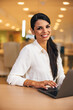 © bnenin - Portrait of a smiling woman, typing on a laptop, sitting at the office.