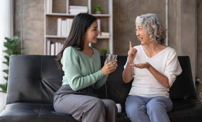 Young Asian woman taking care and giving a glass of water and taken daily medicine or vitamin supplements, elderly healthcare and grandmother.