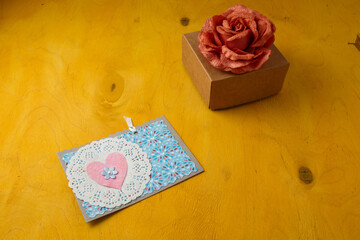 Wall Mural - Blue postcard with pink heart, box and fabric rose flower on bright yellow background. Valentines day, birthday present