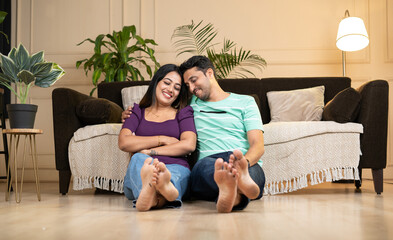 wide shot of happy smiling indian couple embracing each other by eyes closed at home while sitting on floor - concept caring husband, newly married couples and relationship bonding