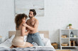 shirtless man in jeans seducing tattooed young woman in night dress sitting on bed.