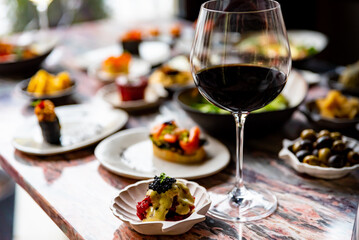 glass with red wine and wine snack set, food from spain, cheese, meat, vegetables and other appetizers on table